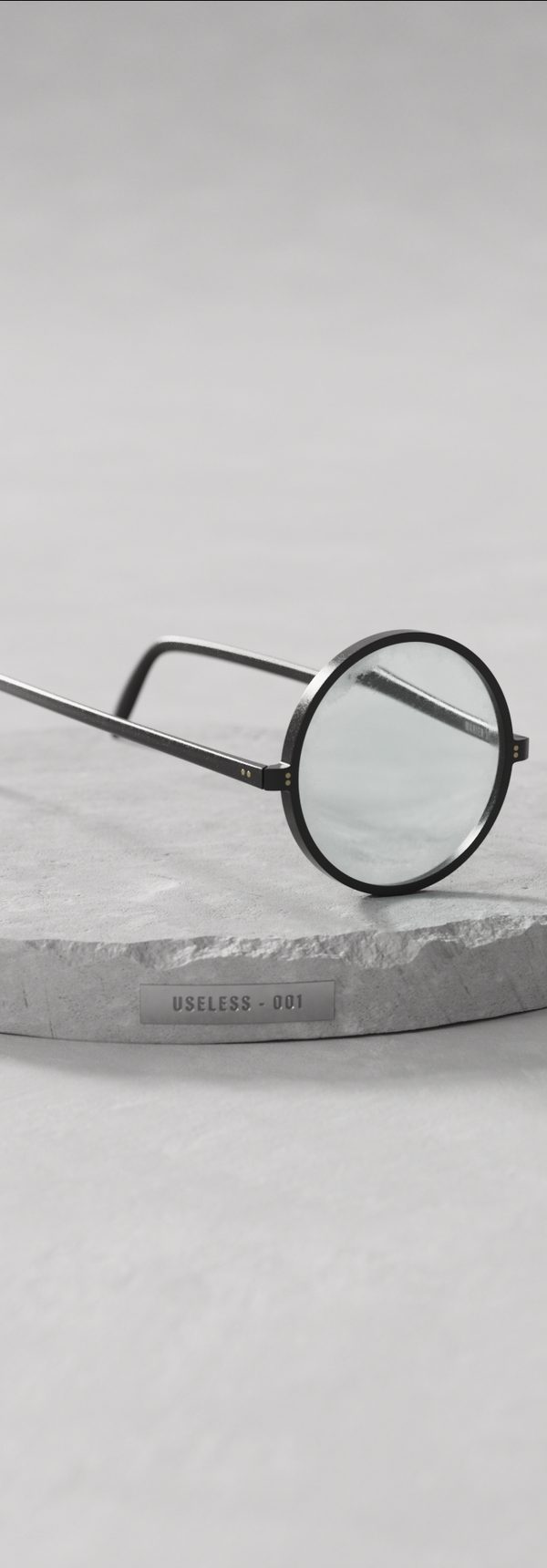 Round glasses resting on a stone plinth labelled Useless 001